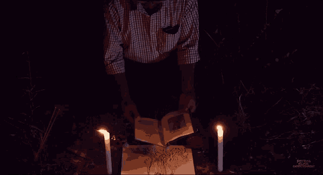 a man is reading a book surrounded by lit candles and a sign that says ' perched ' on it