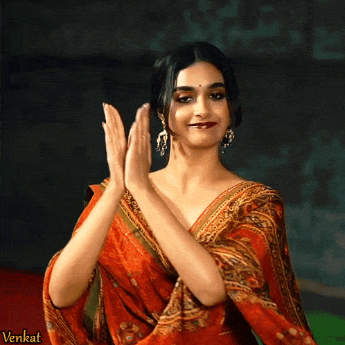 a woman in a red saree is clapping her hands in front of a sign that says " venkat "