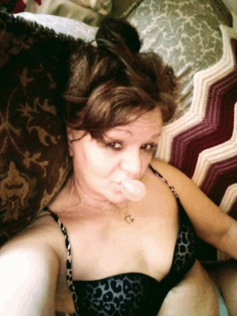 a woman in a black bra is blowing a bubble in her mouth