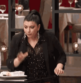 a woman in a black jacket is standing in front of a table with a plate of food on it