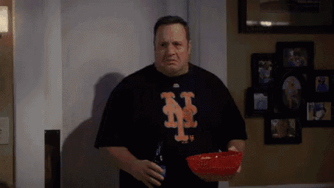 a man wearing a new york mets t-shirt is holding a bowl of popcorn and a bottle of beer .