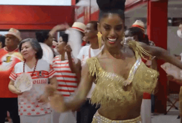 a woman in a gold outfit is dancing in front of a crowd wearing a red and white striped shirt that says " ouba "