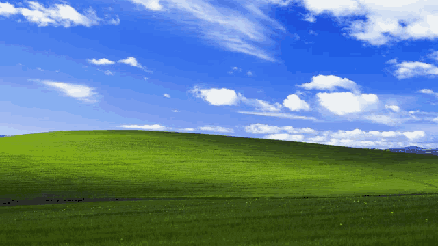 a grassy hill with a blue sky and clouds in the background