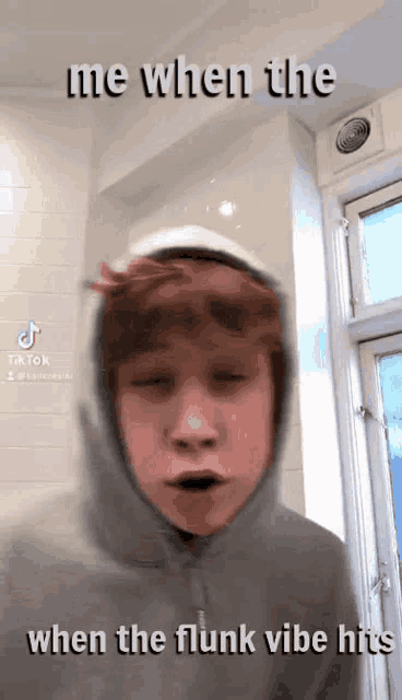 a young man wearing a hoodie is making a funny face while standing in front of a window .