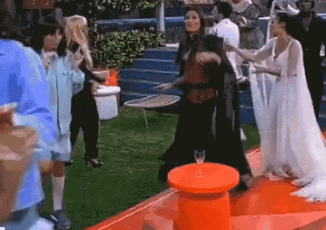 a group of women are dancing on a red carpet in front of a table with a glass of wine on it .