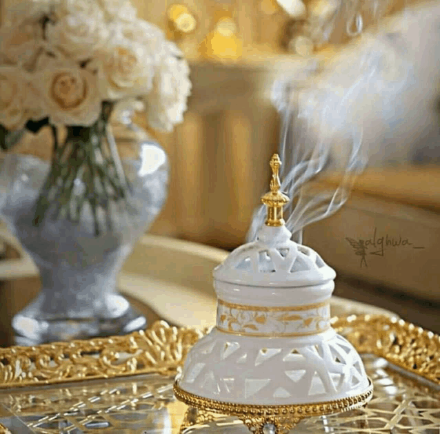 a vase of flowers sits on a table next to a white and gold container