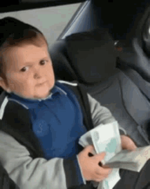 a young boy is sitting in the back seat of a car holding a stack of money and a book .