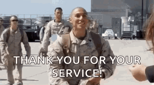 a group of soldiers are walking down a runway and a woman is giving them a thank you for their service sign .