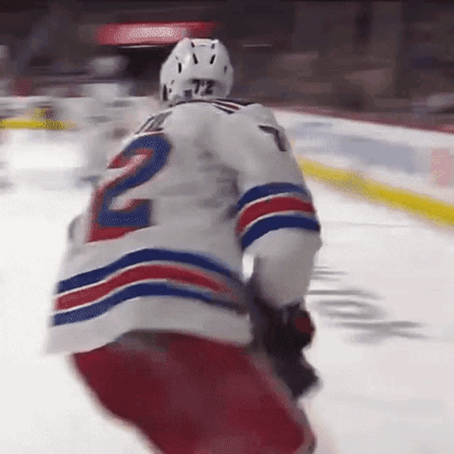 a hockey player wearing a white jersey with the number 2 on it is standing on the ice .