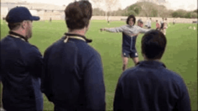 a group of men are standing on top of a soccer field watching a player .