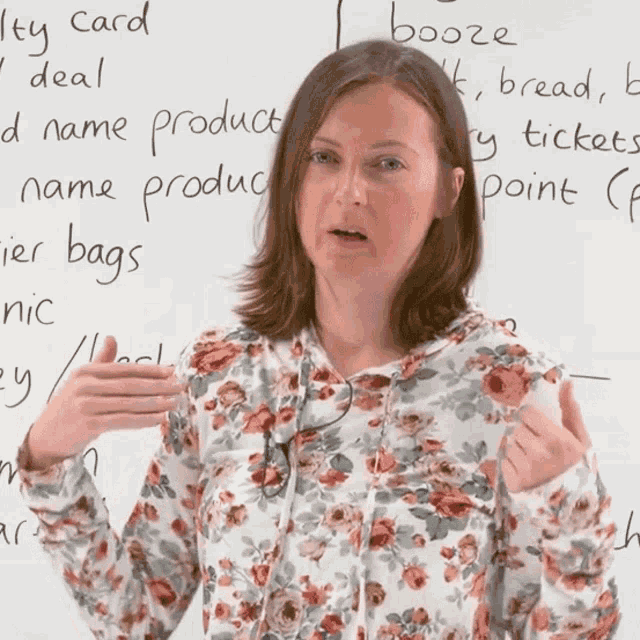 a woman in a floral shirt is standing in front of a white board with the words booze written on it