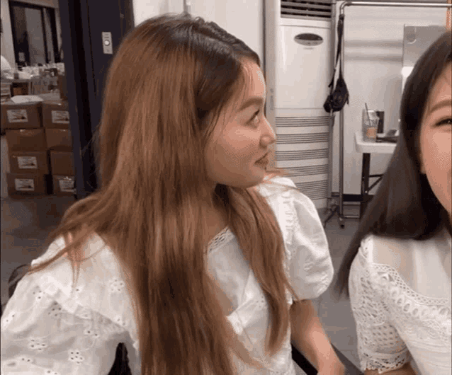 two women are looking at each other in front of an air conditioner that says ' mitsubishi ' on it