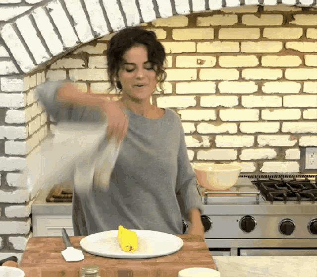 a woman is standing in front of a brick wall in a kitchen with a plate of food on the counter