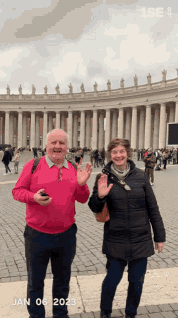 a man in a pink sweater and a woman in a black coat are standing in front of a building with the date jan 06 2023