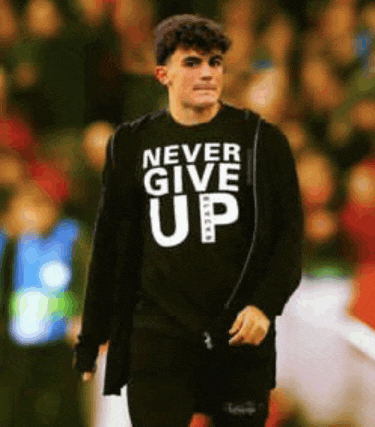 a man wearing a black shirt that says never give up is walking on a field .