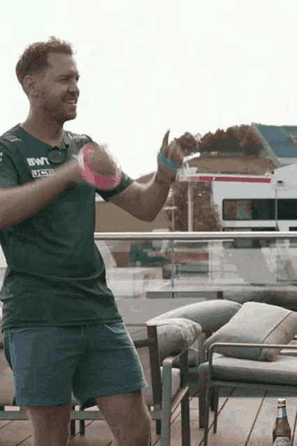 a man in a green shirt and blue shorts is dancing on a balcony with a bottle of beer .