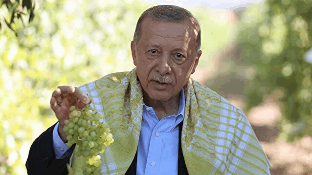 a man with a scarf around his neck is holding a bunch of green grapes