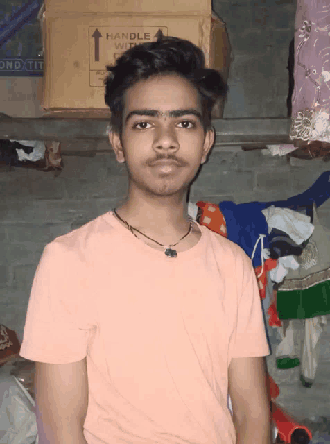 a young man in a pink shirt is standing in front of a cardboard box that says handle with care