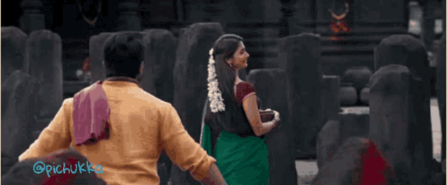 a man and a woman are holding hands in front of a temple . the woman is wearing a green saree .