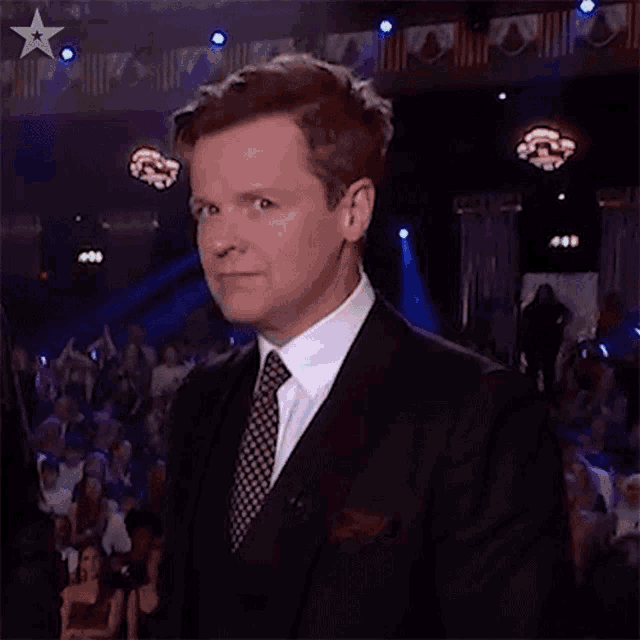 a man in a suit and tie is standing in front of a crowd of people in a theater .