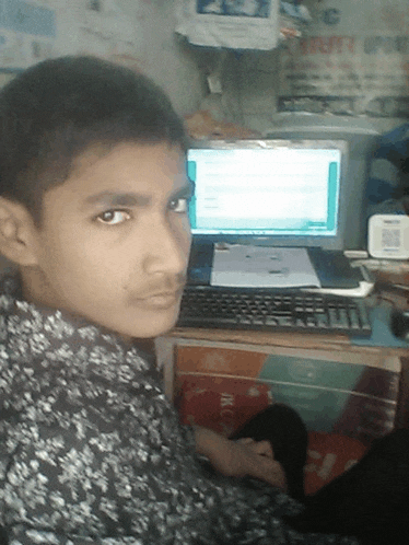 a young boy sitting in front of a computer with a sign behind him that says ' jkc '