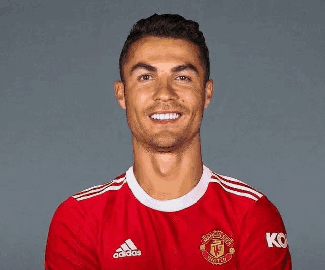 a man wearing a red adidas manchester united jersey smiles for the camera