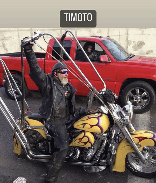 a man riding a motorcycle with a red truck in the background that says timoto on it