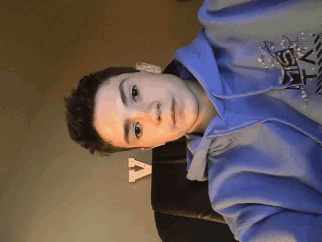 a young boy wearing a blue hoodie with the letter a on the wall behind him