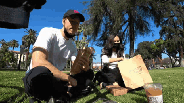 a man and a woman are sitting in the grass with a bag that says ' baked beans ' on it