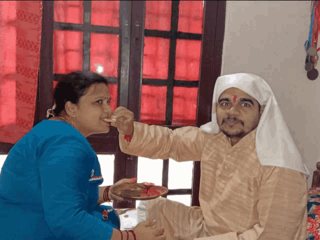 a woman in a blue shirt is feeding a man with a plate of food