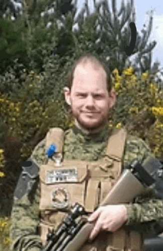 a man in a military uniform is holding a rifle in front of a bush .