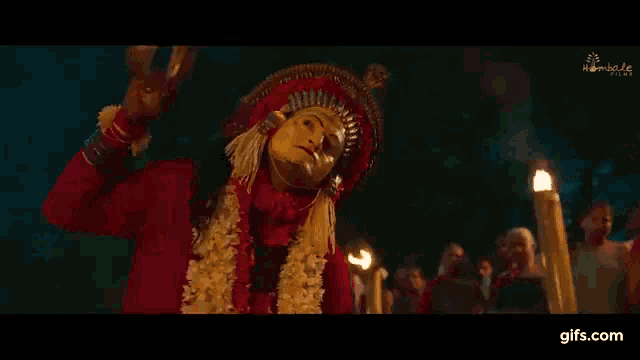 a man in a red and gold costume is dancing in a dark room with candles in the background .