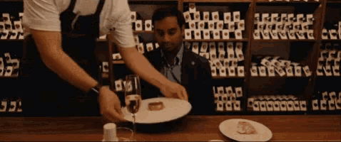 a man sits at a table with a plate of food and a glass of wine while a waiter serves him