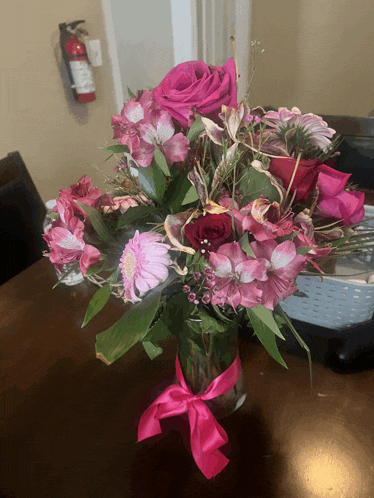 a vase of pink flowers with a pink ribbon