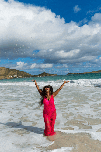 a woman in a red dress is standing in the ocean with her arms outstretched