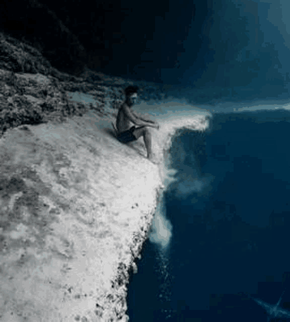 a man is sitting on a cliff in the ocean .