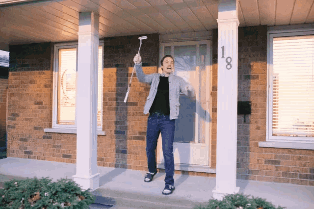 a man stands on a porch holding a remote control in front of a house with the number 18 on it