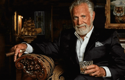 a man in a suit is sitting in a chair holding a glass of whiskey and a cigar