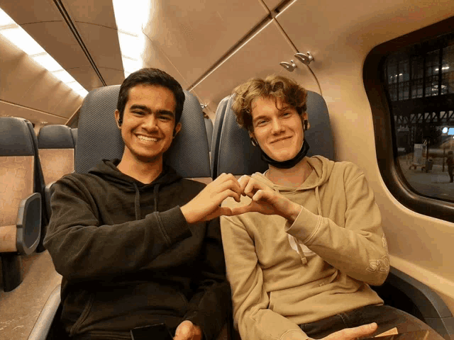 two men are making a heart shape with their hands