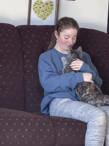 a girl sitting on a couch holding a cat in her lap