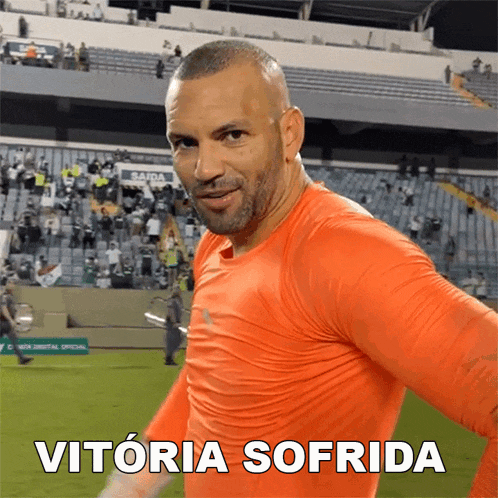 a man in an orange shirt is standing in front of a stadium with the words vitoria sofrida written on the bottom