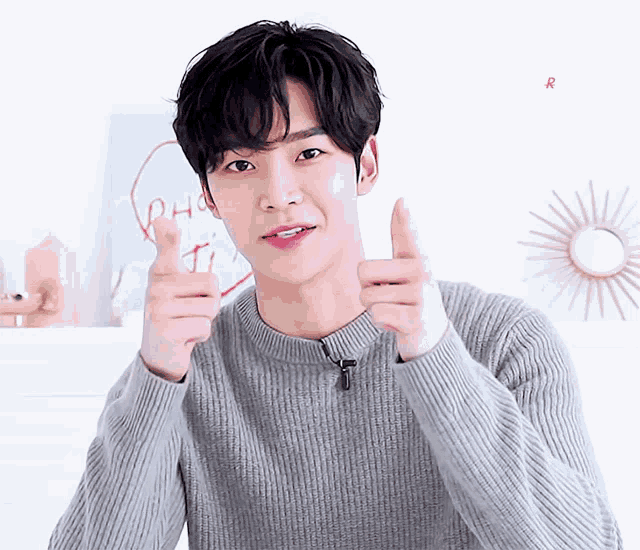 a young man wearing a grey sweater giving a thumbs up