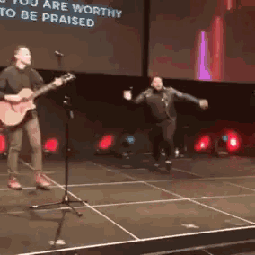 a man playing a guitar on a stage with the words " you are worthy to be praised " on the screen