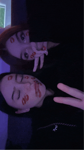 two girls with red lips painted on their faces giving a peace sign