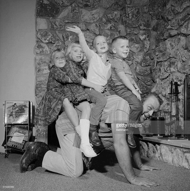 a black and white photo of a man kneeling down with his children on his shoulders