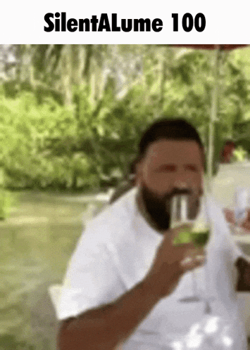 a man with a beard is drinking a glass of wine while sitting on a table .