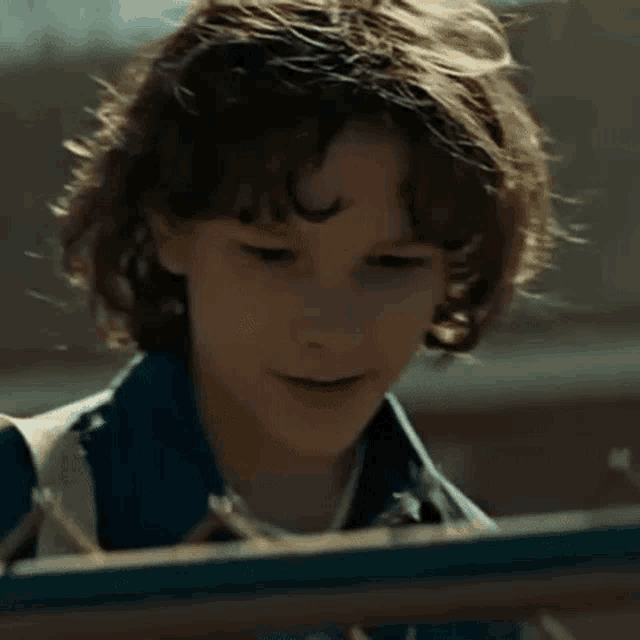 a young boy with curly hair is standing next to a fence and smiling .