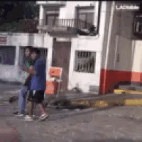 a man in a blue shirt is walking down a street in front of a building with red and white paint .