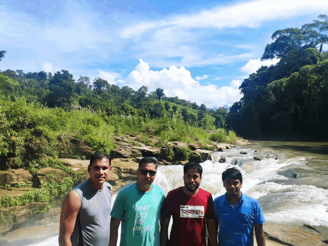 four men standing in front of a waterfall one of them is wearing a shirt that says " i beat and i am ugly "