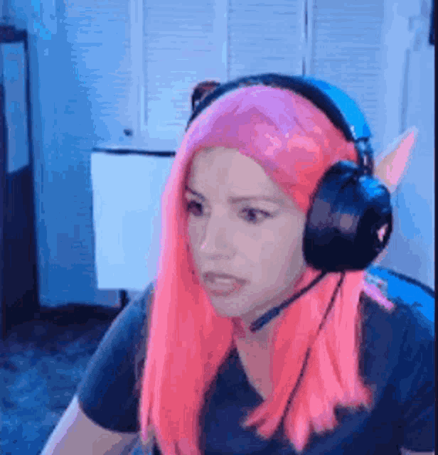 a woman with pink hair and headphones is sitting at a computer .